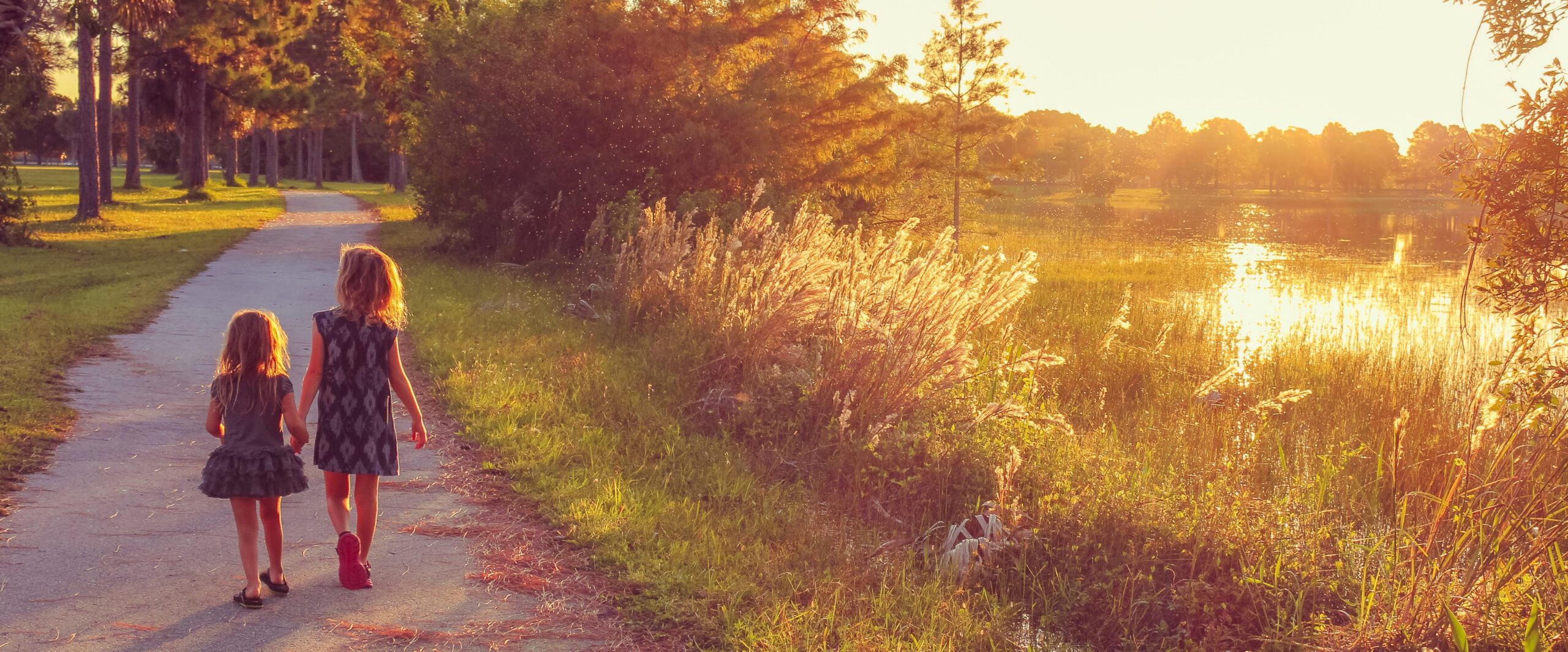 Two children walking beside a lake at sunset